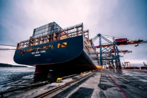 Shipping container vessel alongside quay with cranes unloading boxes